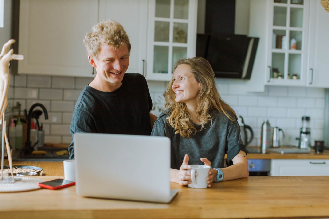 A couple laughing together at the kitchen table with a laptop